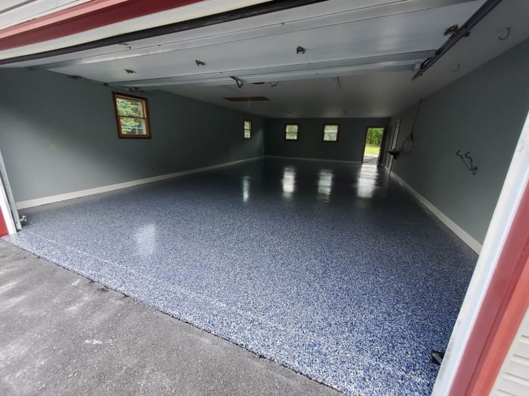 Empty garage interior with gray epoxy flooring, dark walls, and red framing around the open door