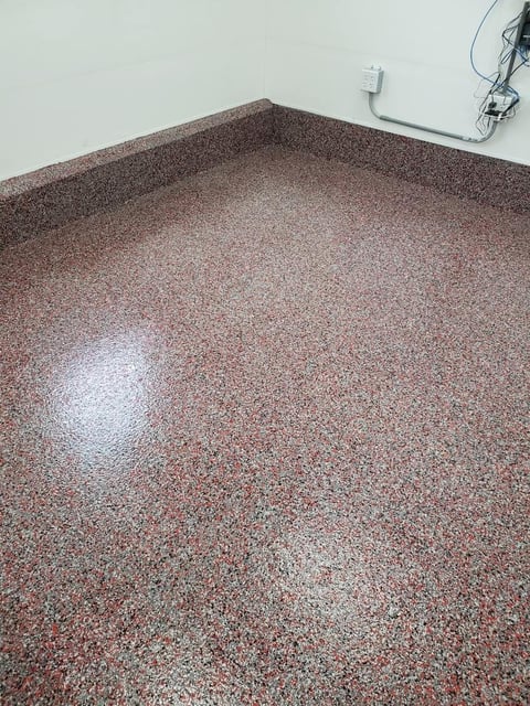 Speckled brown and red epoxy flooring in an empty room with white walls and electrical outlet