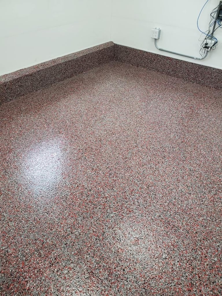 Speckled brown and red epoxy flooring in an empty room with white walls and electrical outlet