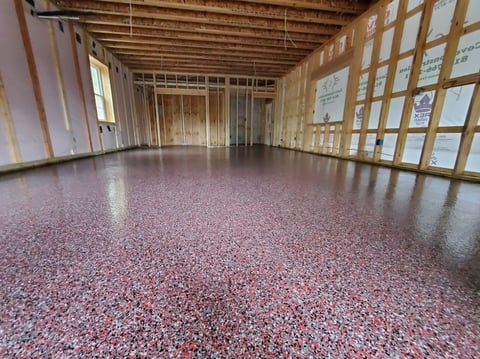 Empty warehouse interior with exposed wooden framing, drywall walls, and speckled pink and white epoxy flooring